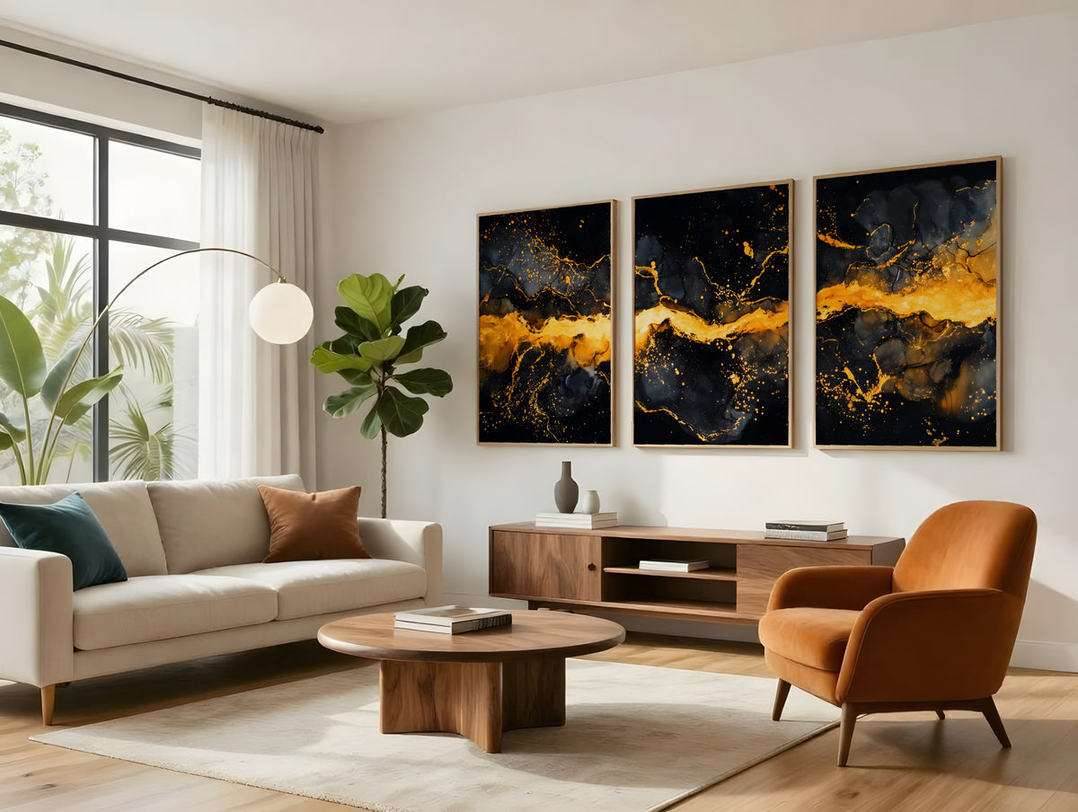 Black and gold abstract triptych in light wood frames hung above a walnut sideboard in a bright living room with a fiddle leaf fig and cream sofa
