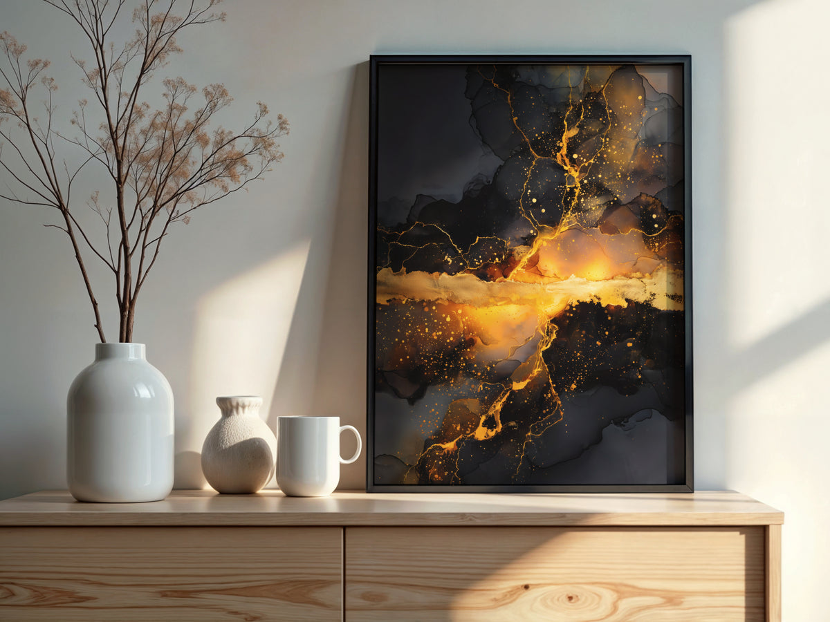 Black and gold abstract art print in a slim dark frame resting on a pale wood sideboard beside white ceramic vases and dried branches